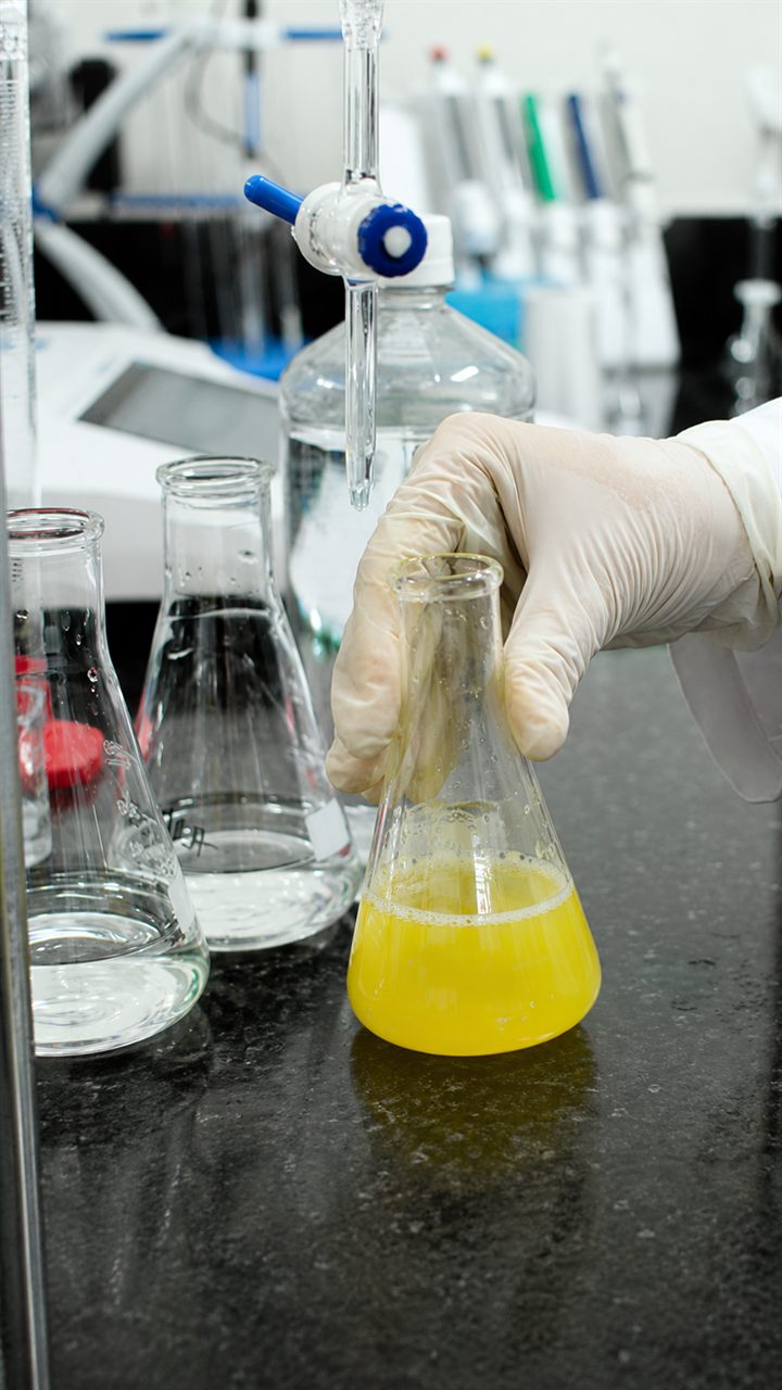 Analista do laboratório LabLAAE manipulando amostra em frasco Erlenmeyer durante análise química